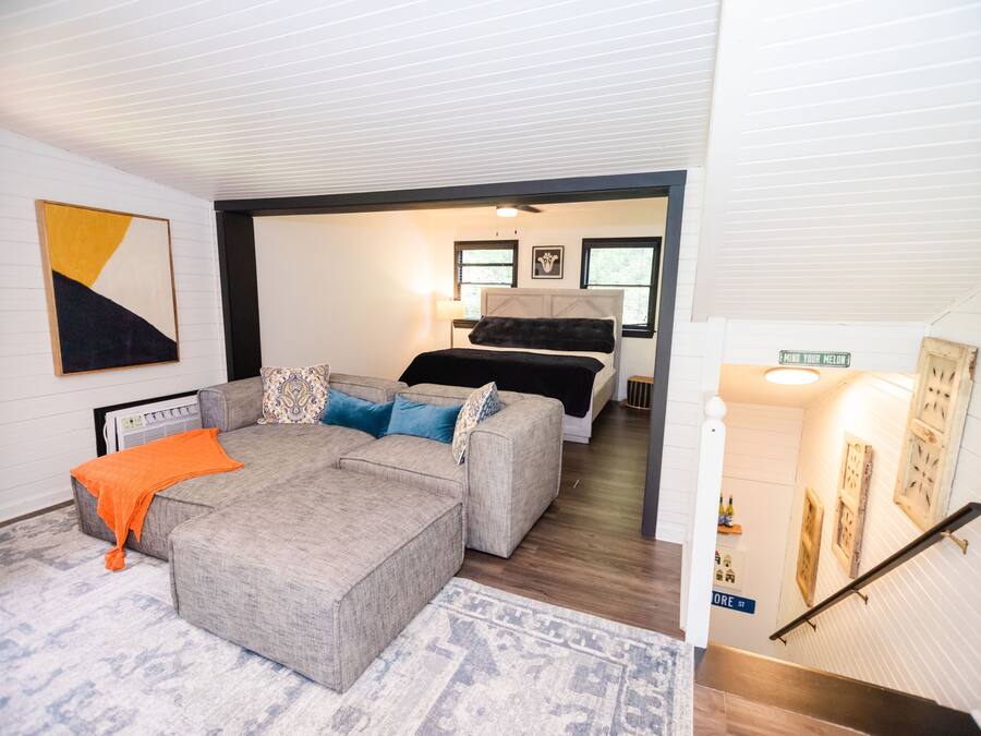 A modern living room with a sectional sofa, a bed, and a staircase leading to another level.