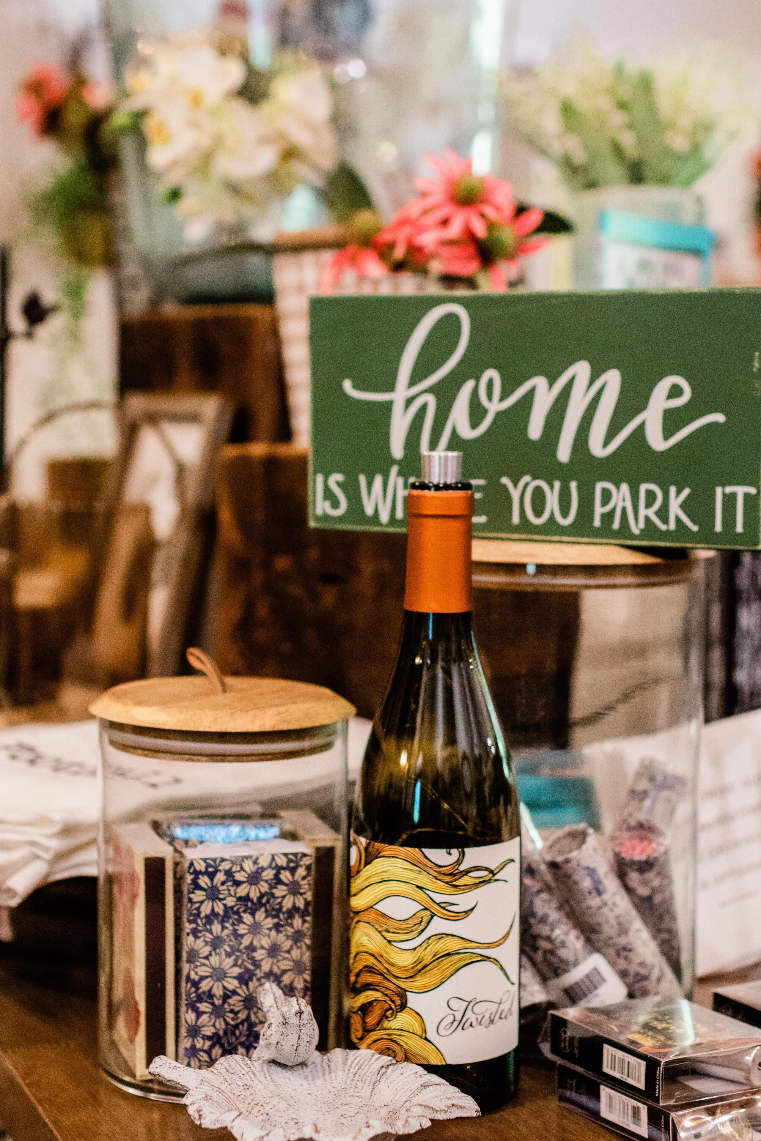 Una botella de vino, una vela decorativa y un cartel que dice 'hogar es donde lo aparcas'.