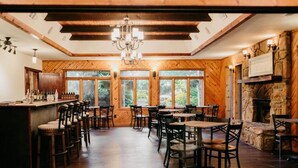 A rustic interior with wooden walls, a stone fireplace, and a bar area with stools and tables. - Sylvan Valley Lodge & Cellars (Sautee Nacoochee)