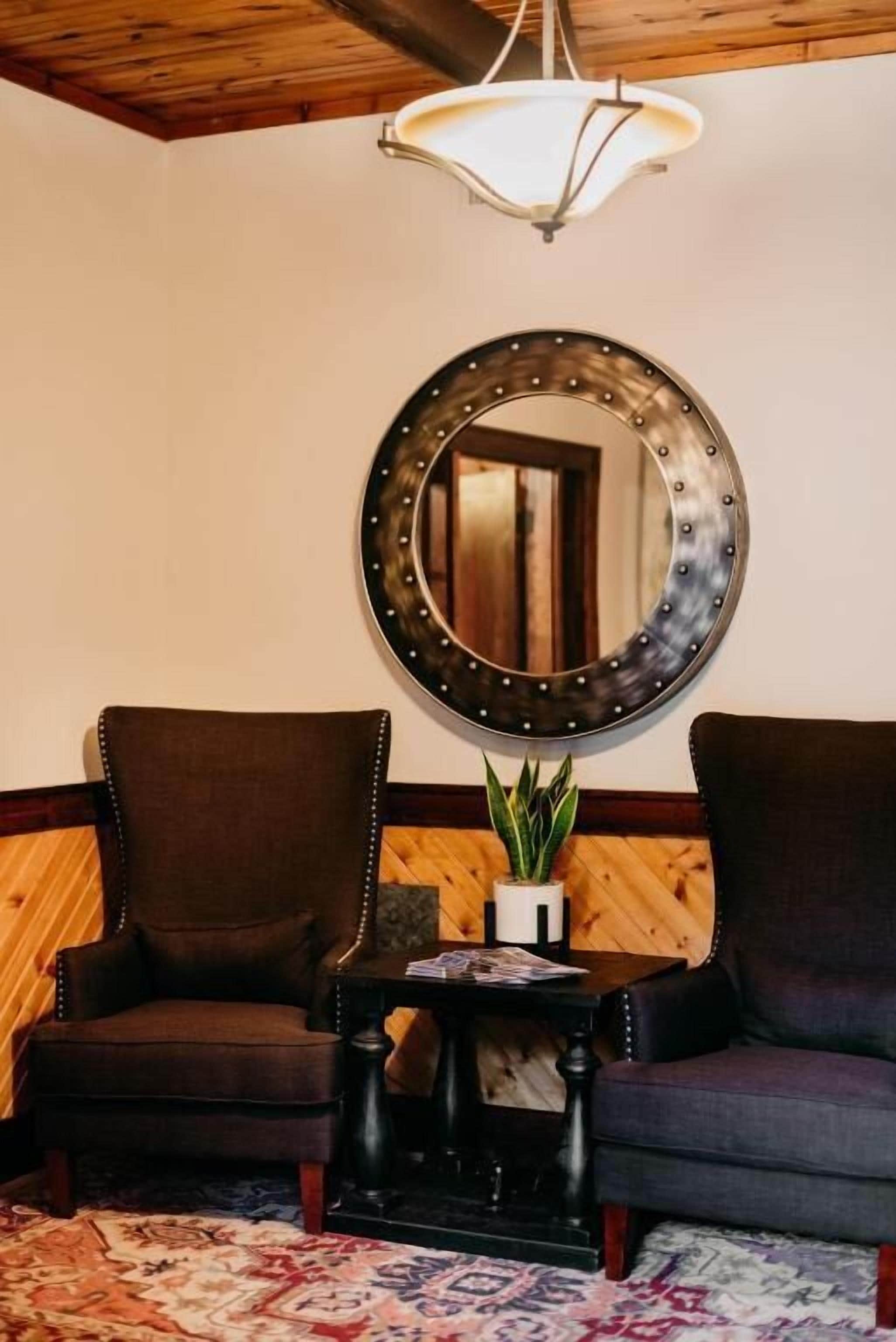 A room with two dark armchairs, a small table with a plant, and a large mirror on the wall.