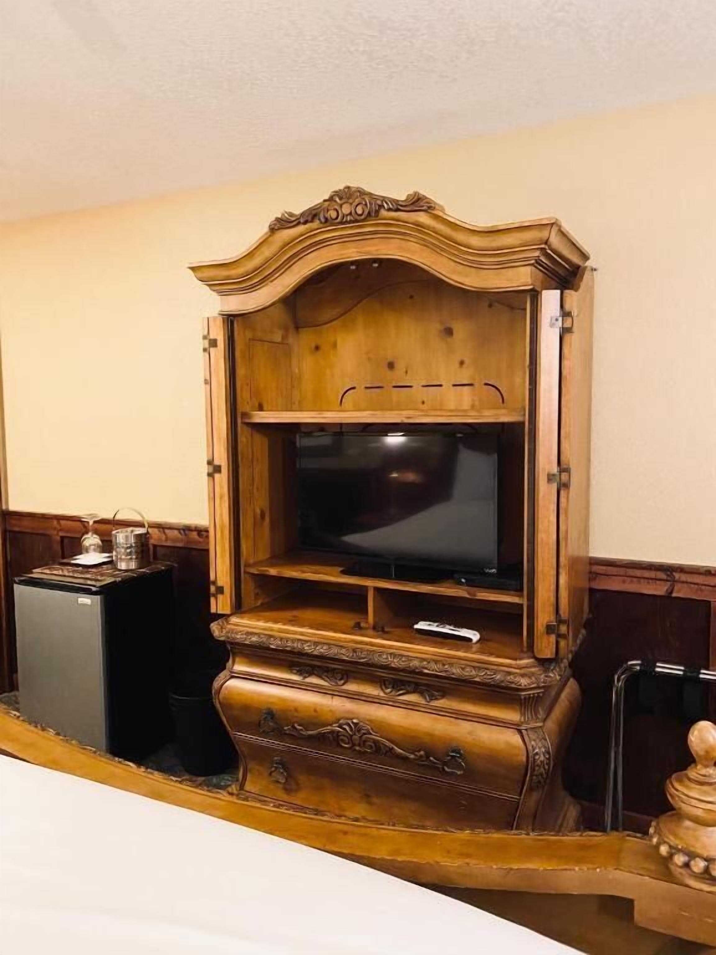 A wooden cabinet with a television, a small refrigerator, and a microwave.