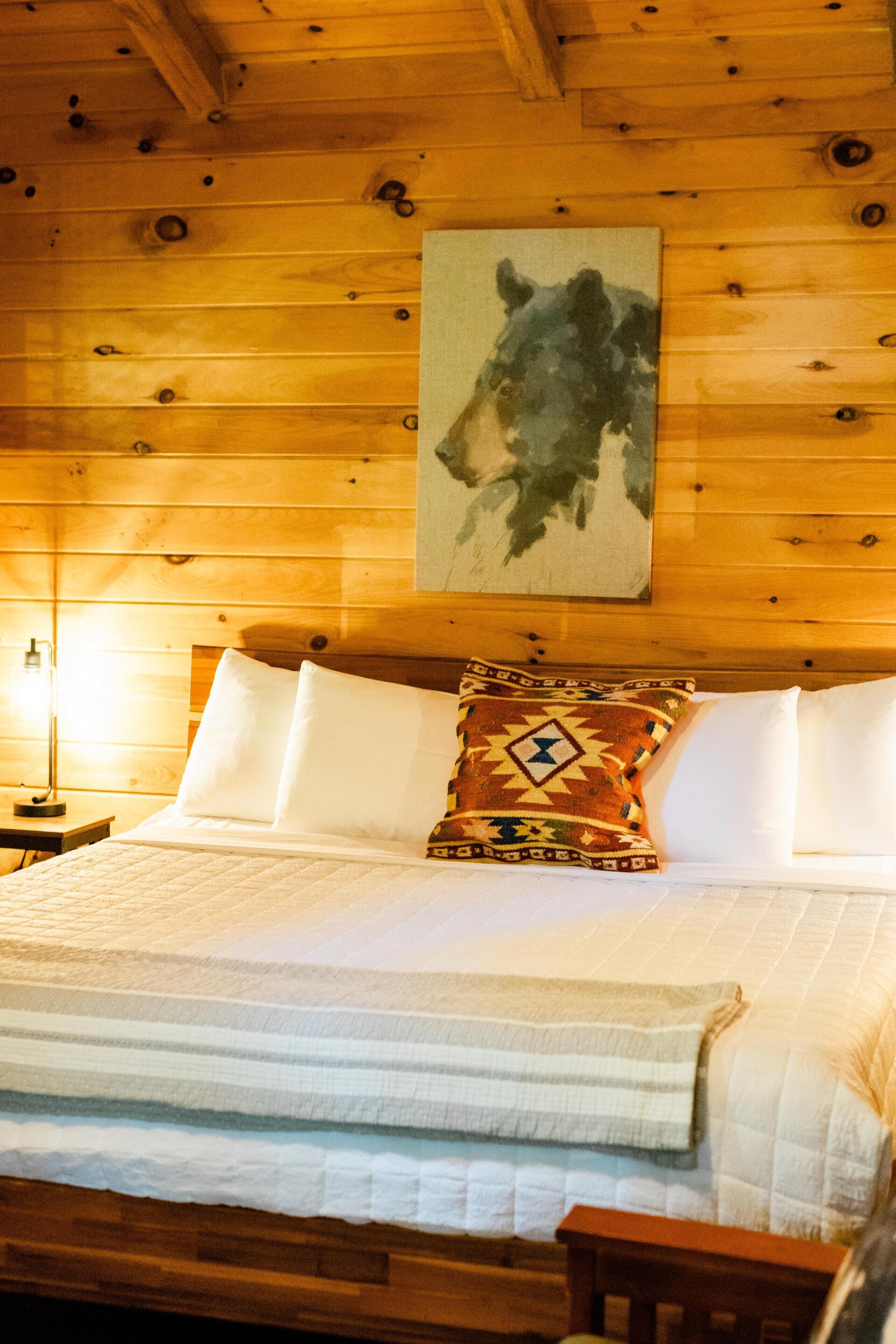 Ein holzgetäfeltes Zimmer im Chalet-Stil mit einem Bett, einem Nachttisch und einem an der Wand hängenden Gemälde.