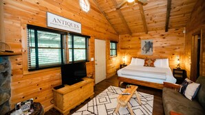 A wooden cabin room with a bed, a television, and a sign reading "ANTIQUES". - Sylvan Valley Lodge & Cellars (Sautee Nacoochee)