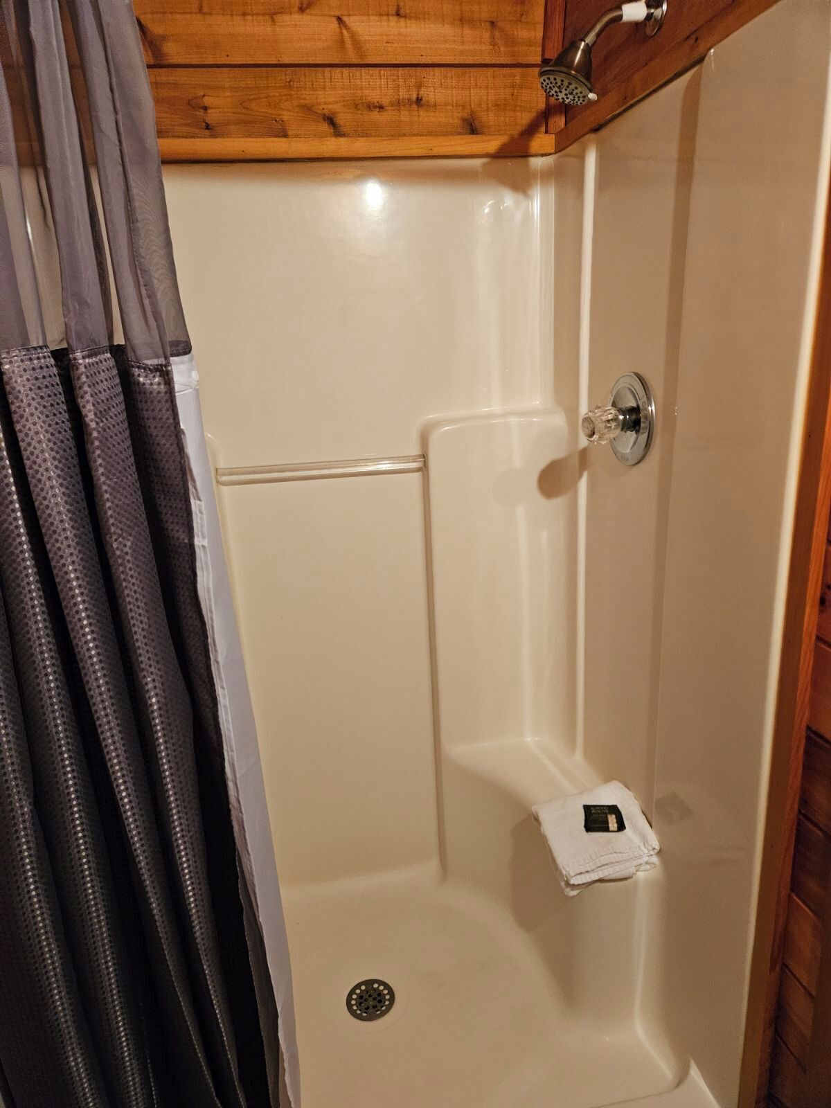 Een douchegedeelte met een houten plafond, een douchekop en een klein handdoekrek.