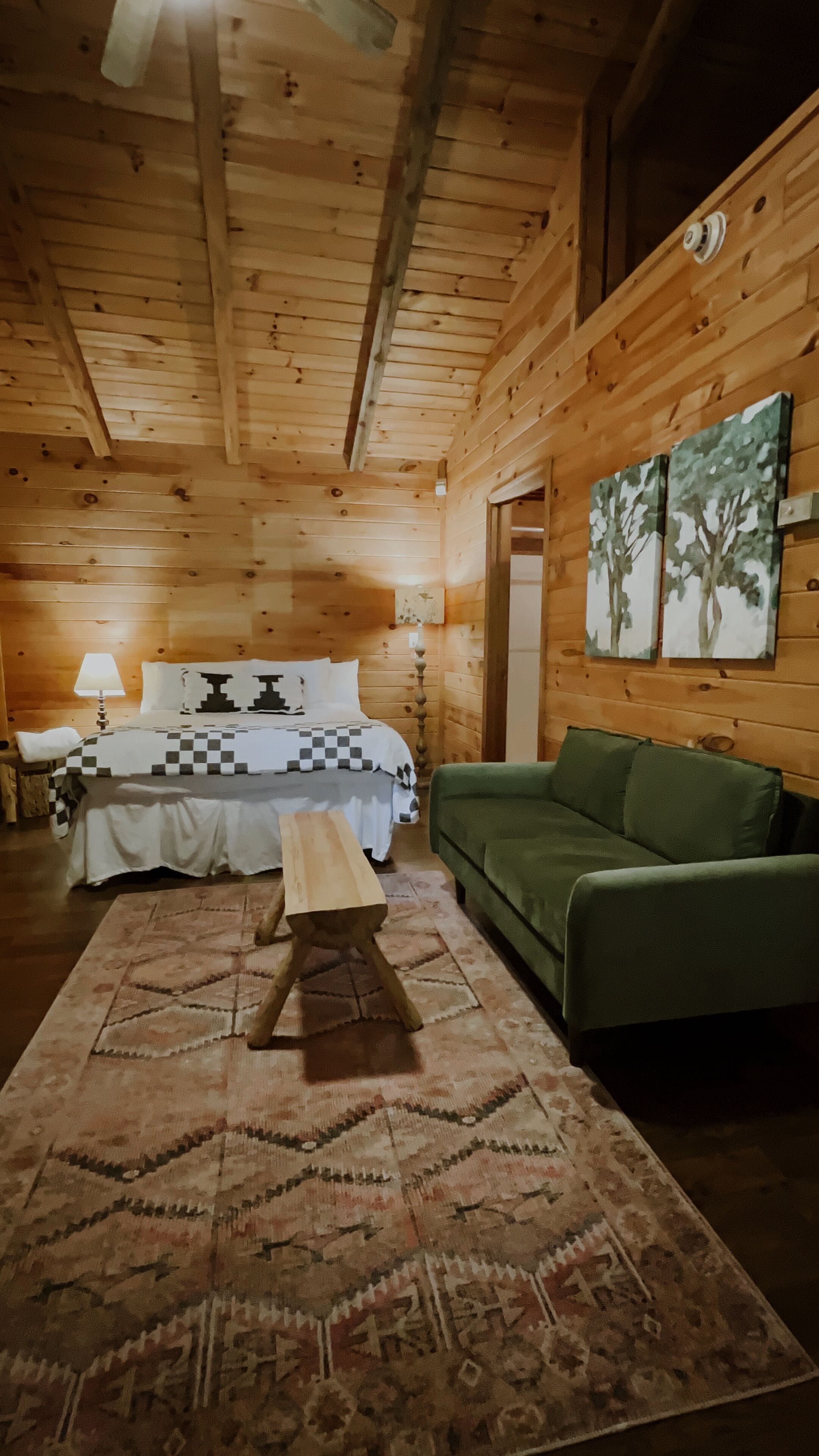 Una habitación tipo cabaña de madera con una cama, un sofá verde, un tapete estampado y paredes de madera.