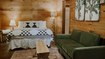 Una habitación tipo cabaña de madera con una cama, un sofá verde, un tapete estampado y paredes de madera.
