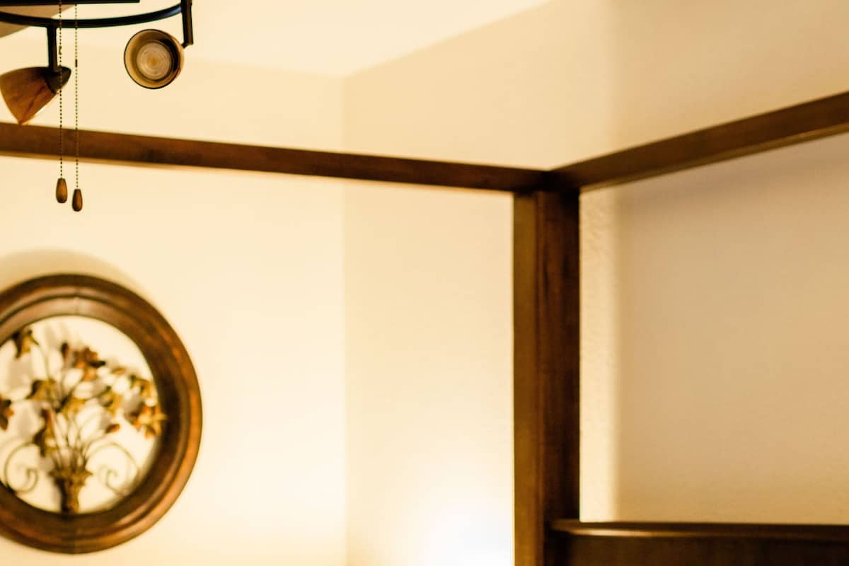 Una cama bien hecha con almohadas estampadas con motivos florales, un cabecero de madera y un espejo redondo montado en la pared.