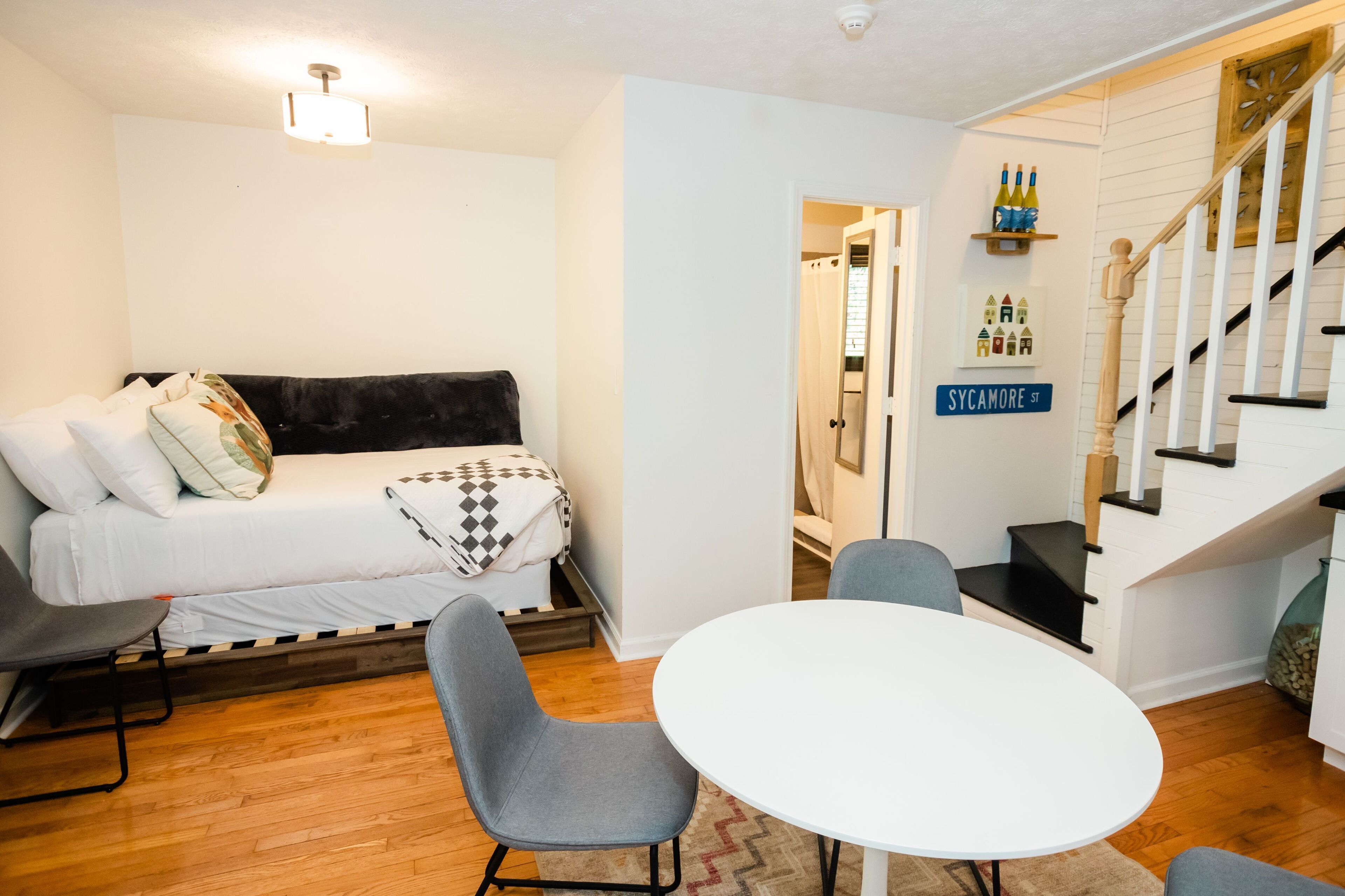 Una habitación con cama, una mesa redonda, dos sillas, una escalera y un estante en la pared con botellas.