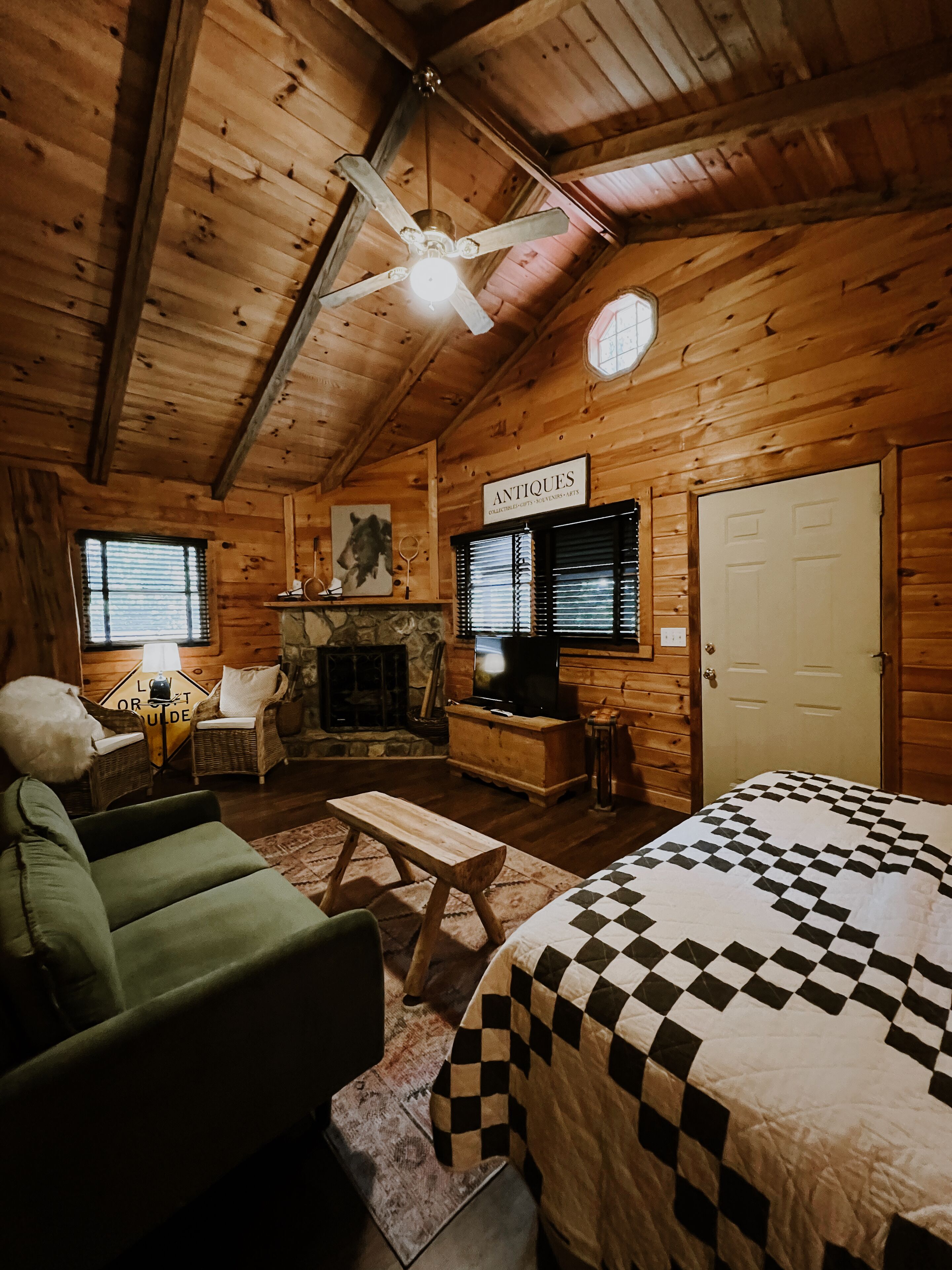 L’intérieur d’un chalet confortable, avec une cheminée, un téléviseur, un lit recouvert d’une couverture à carreaux et une pancarte indiquant « ANTIQUITÉS ».