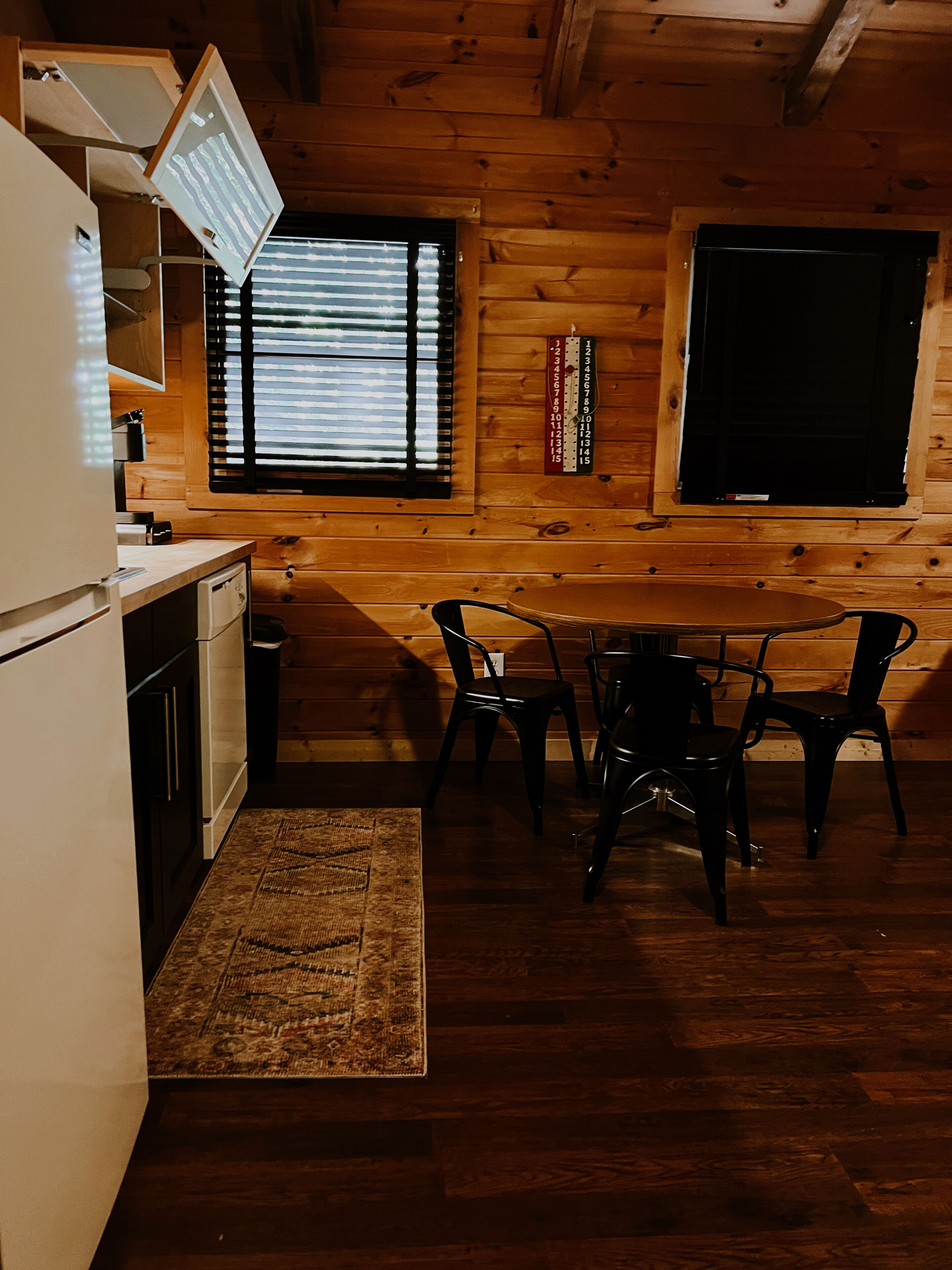 Interior de uma cabana de madeira com cozinha, área de refeições e uma janela grande.