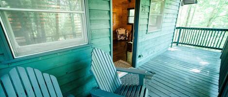 Une cabane en bois avec une véranda, deux fauteuils Adirondack et une petite chaise à l’intérieur.