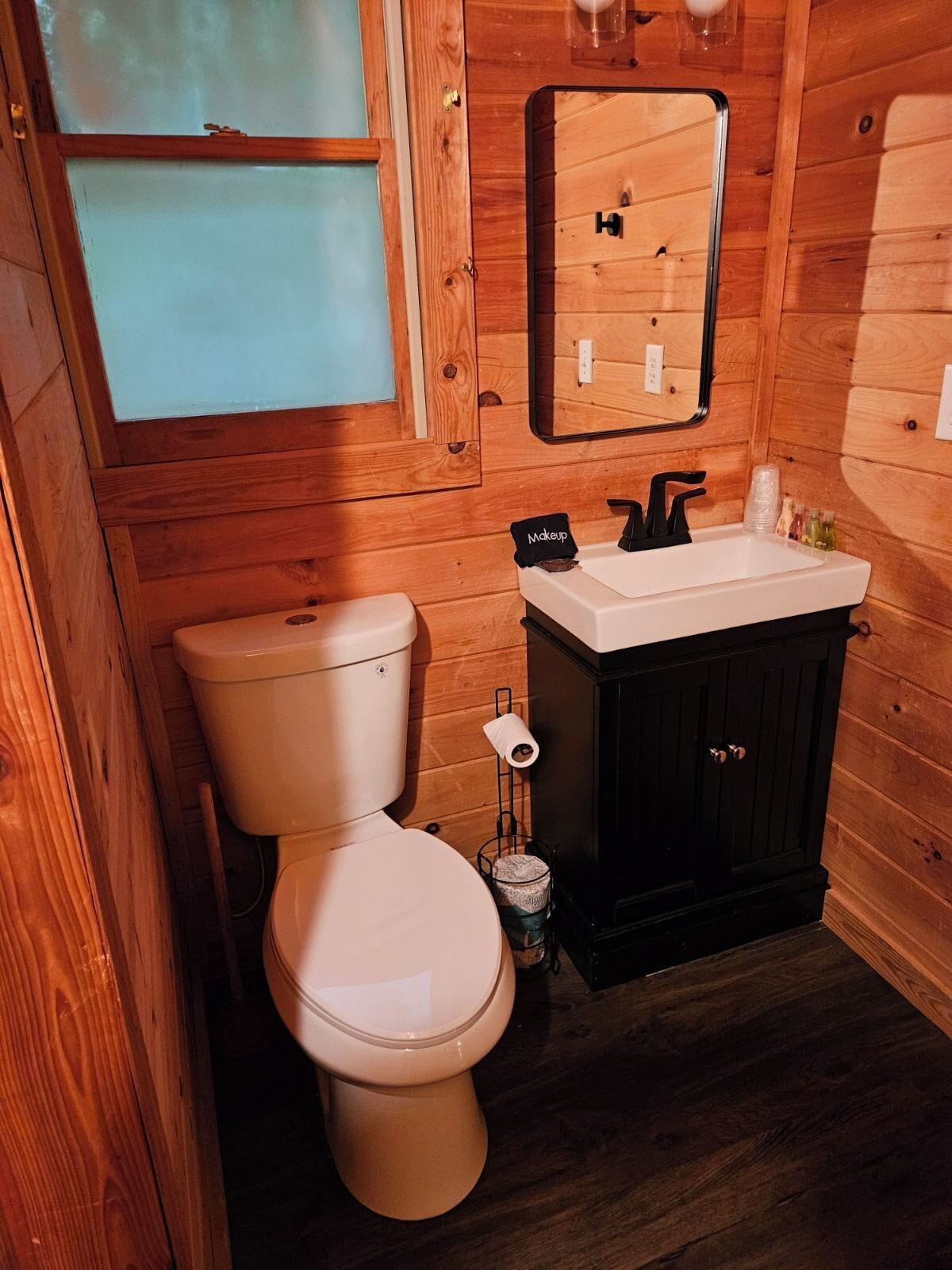 Ein kleines Badezimmer aus Holz mit Toilette, Waschbecken und Spiegel.