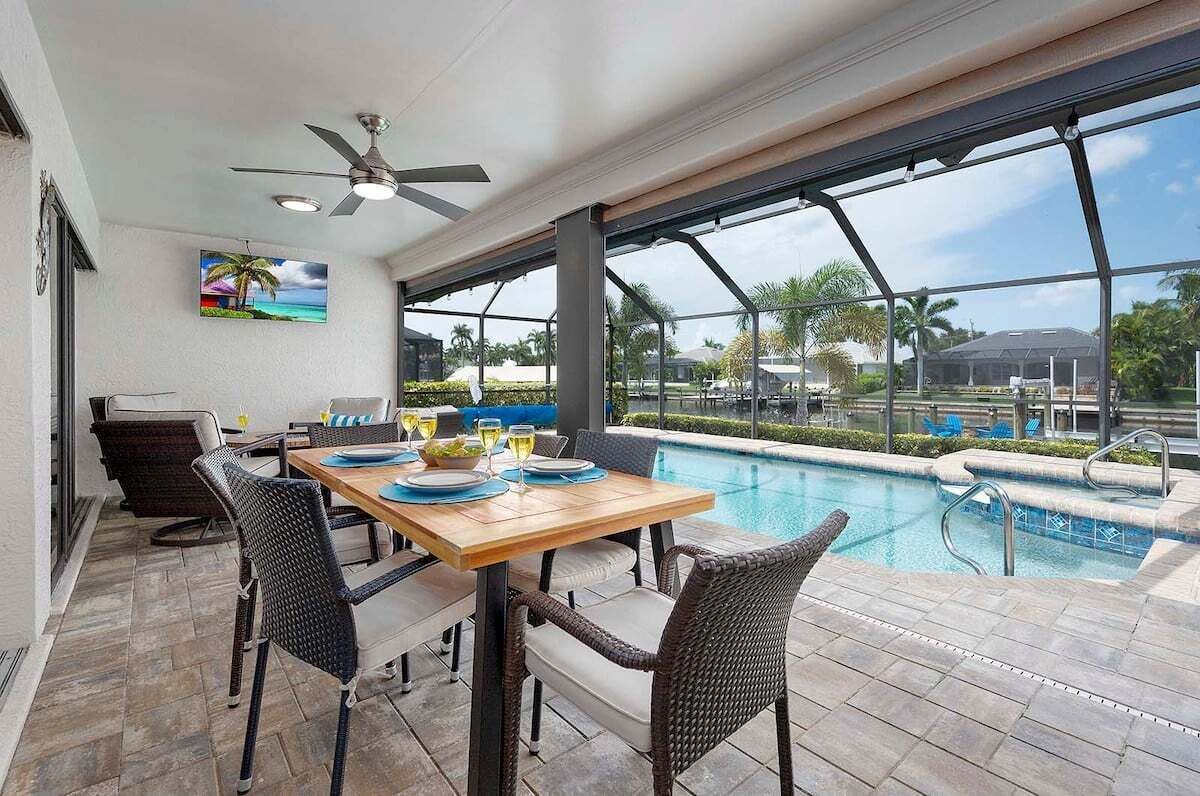 Área de refeições ao ar livre com vista para a piscina, cadeiras de vime, mesa de madeira e ventilador de teto.