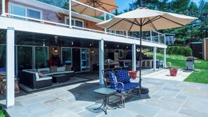 A covered patio with outdoor seating, a glass-enclosed upper level, and a view of a residential area. - Sun Drenched Lakefront Cove (Thompson)