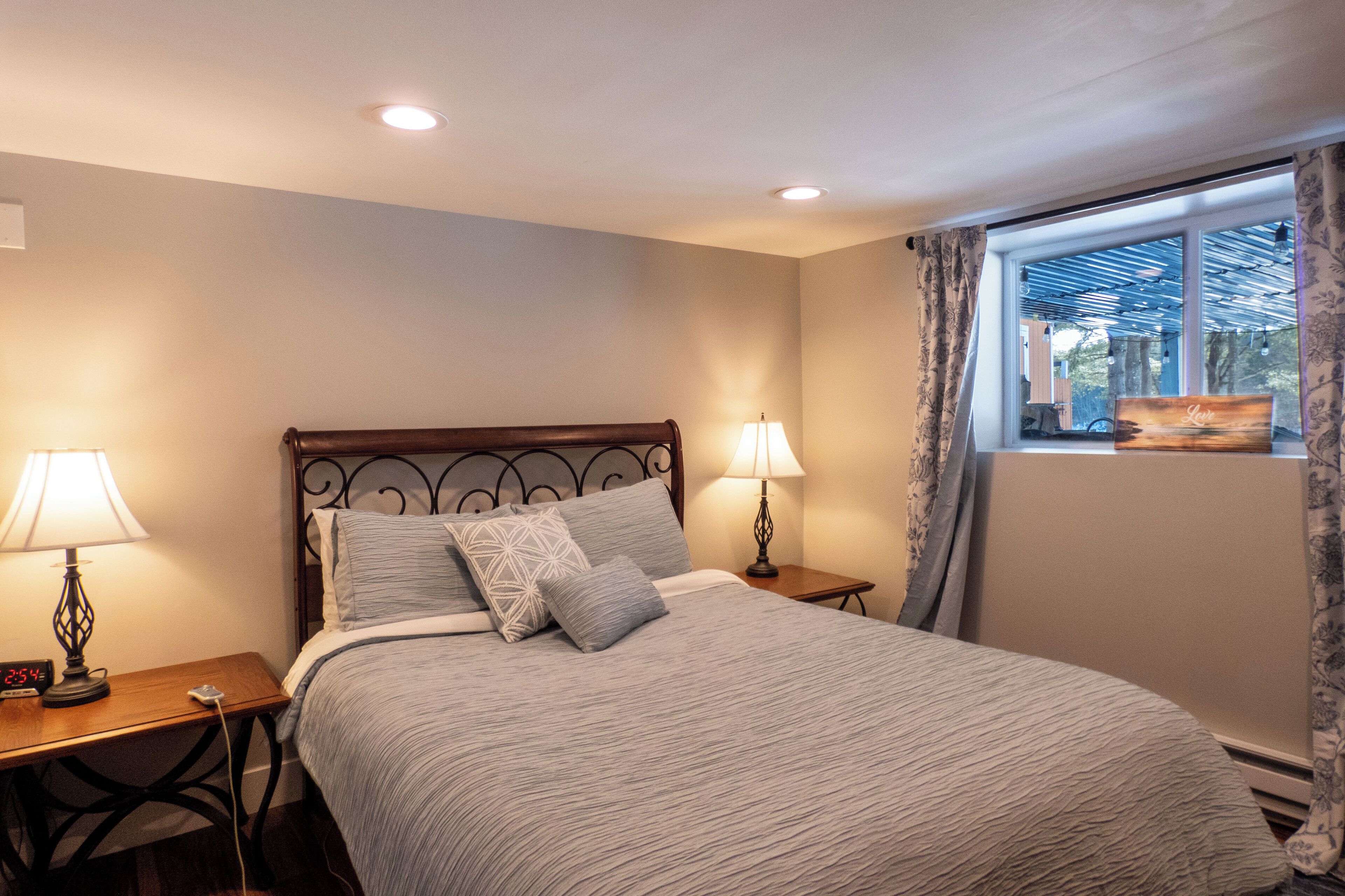 A bedroom with a bed, two bedside tables with lamps, a window with curtains, and a view of the outside.