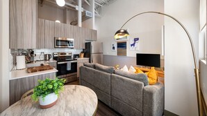 A modern kitchen with stainless steel appliances, a grey sofa, and a round marble table with a plant. - Downtown Mich Ave #10 | gym+rooftop (Chicago)