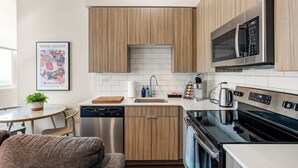 A modern kitchen with wooden cabinets, stainless steel appliances, and a small dining area with a table and chairs. - Downtown Mich Ave #10 | gym+rooftop (Chicago)