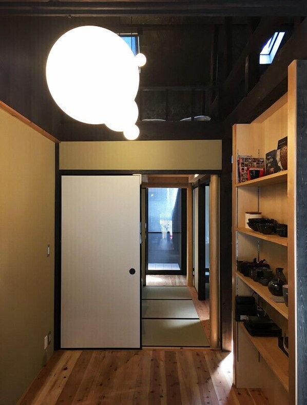 A narrow hallway with a wooden floor, a white door, and a shelf with various items.