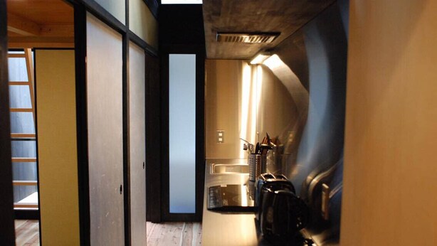 A narrow hallway with a kitchen area on the right, featuring a sink, stove, and coffee machine.