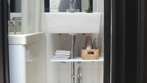 A compact bathroom with a white sink, a mirror, and a shower.