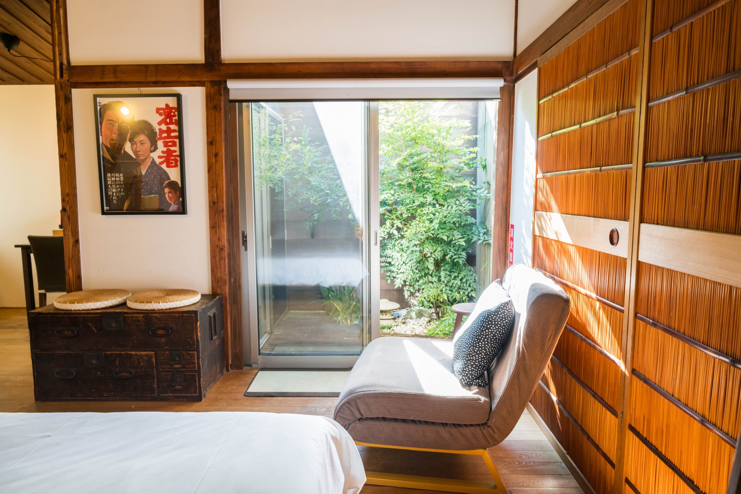 A room with a bed, a chair, a wooden cabinet, and a poster on the wall.