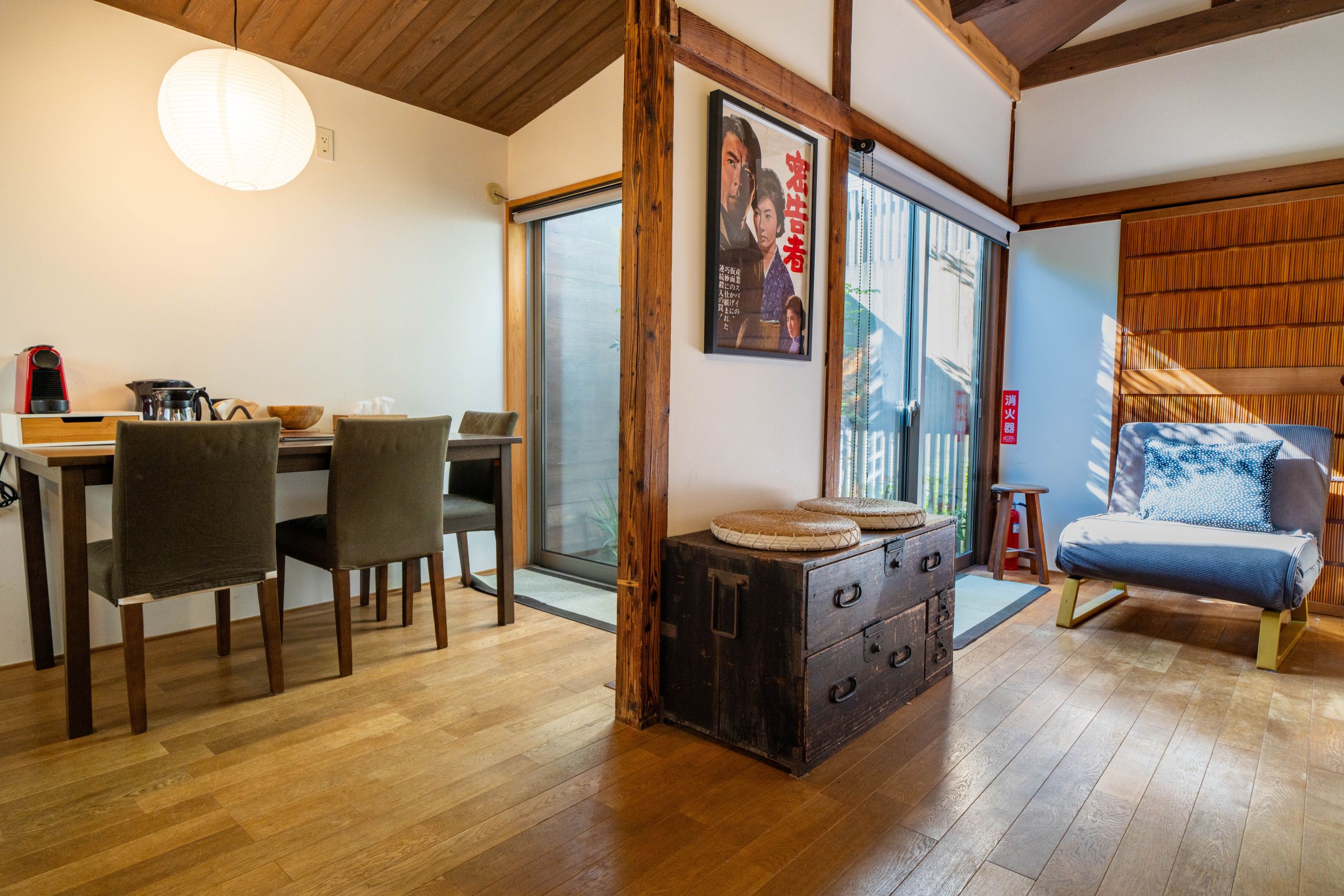 A traditional Japanese-style room with a wooden floor, a dining table with chairs, a sofa, a cabinet, and a large window.