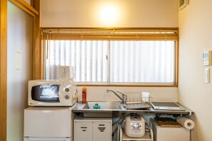 A compact kitchenette with a microwave, a small refrigerator, a sink with a drying rack, and a window with blinds. - Ikebukuro Nigo - Tokyo architectural small villa (Tokyo)