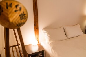 A bedroom with a bed, a bedside table, and a wooden object with a light on it. - Ikebukuro Nigo - Tokyo architectural small villa (Tokyo)