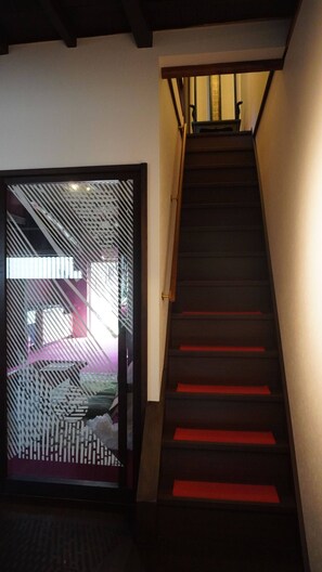 A staircase with a wooden handrail and red carpeted steps leading to a room with a sliding door.