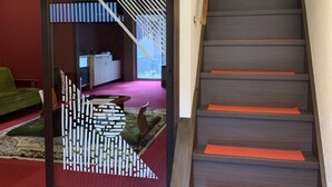 Een trap met donkere treden en rode treeplanken, die leidt naar een kamer met een patroon vloer en een groene bank.