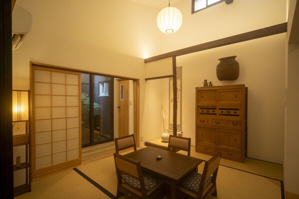 A traditional Japanese room with tatami flooring, a sliding door, a table with chairs, a cabinet, and a hanging light fixture.
