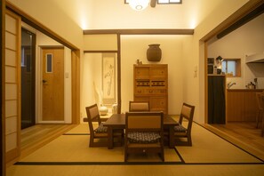 A traditional Japanese-style room with tatami flooring, a low table with chairs, a cabinet with decorative items, and a sliding door.