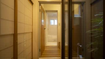 A hallway with a wooden floor, a glass door, and a view into a room with a bathtub.