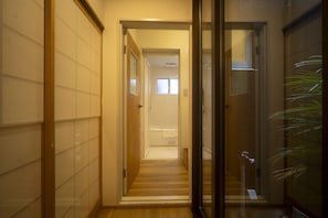 A hallway with a wooden floor, a glass door, and a view into a room with a bathtub. - Gion House - Renovated traditional house tucked away in Gion (Kyoto)