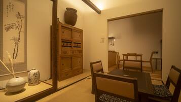 A traditional Japanese room with tatami flooring, a low wooden cabinet, a dining table with chairs, and a large vase.