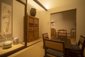 A traditional Japanese room with tatami flooring, a low wooden cabinet, a dining table with chairs, and a large vase. - Gion House - Renovated traditional house tucked away in Gion (Kyoto)