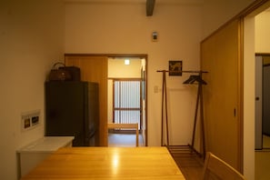 A room with a wooden table, a refrigerator, a hanging coat rack, and a sliding door leading to another room. - Gion House - Renovated traditional house tucked away in Gion (Kyoto)