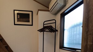 Une pièce avec un escalier en bois, un climatiseur fixé au mur, une fenêtre avec vue et un portant métallique avec des cintres.