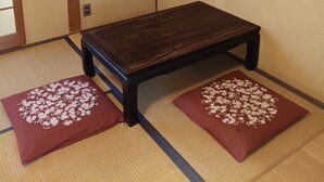 Une pièce de style japonais traditionnel, avec un sol recouvert de tatamis, une petite table en bois et un éventail décoratif accroché au mur.