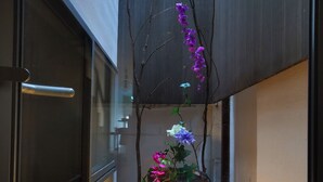 A narrow outdoor corridor with a small garden area featuring a variety of flowering plants and a stone pathway.