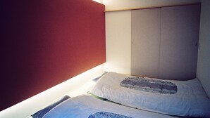 A small, narrow room with a single bed, a red wall, and a white ceiling.