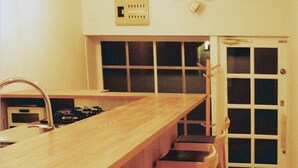 A kitchen with a long wooden countertop, a gas stove, and a stainless steel range hood. There are wooden chairs with black cushions aligned along the countertop.