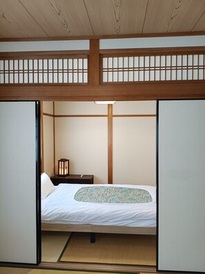 A traditional Japanese-style room with tatami flooring, a low wooden bed, and a shoji screen door.