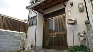 A traditional Japanese building with a large wooden sliding door, a small air conditioning unit, and a stone lantern. - Gion Rokudo - Comfortable house in Gion (Kyoto)