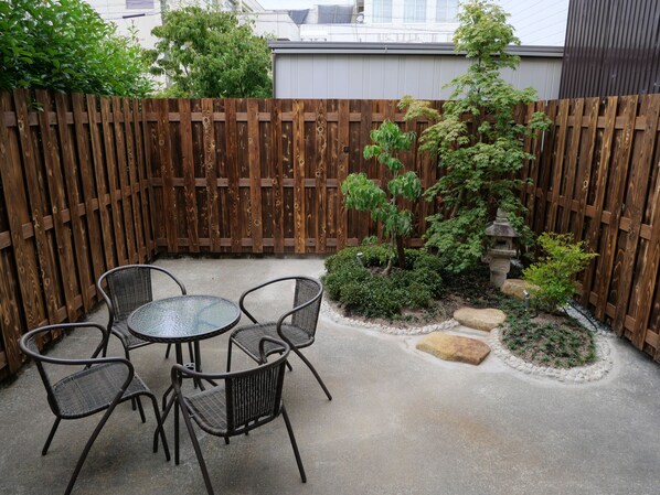 A patio area with a wooden fence, a small garden with a tree and rocks, and a round table with chairs. - Sakura Aburaya - Perfect traditional & comfortable house (Takayama)
