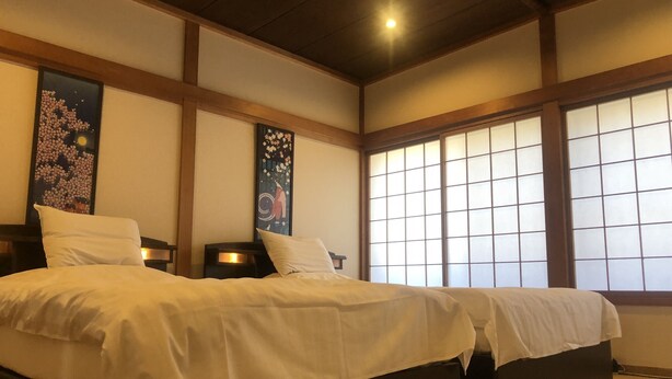 A traditional Japanese-style hotel room with tatami flooring, a large bed with white bedding, and sliding shoji doors. - Sakura Aburaya - Perfect traditional & comfortable house (Takayama)