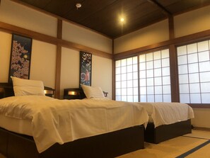 Quarto de hotel tradicional em estilo japonês, com piso de tatame, uma cama grande com roupa de cama branca e portas deslizantes shoji.
