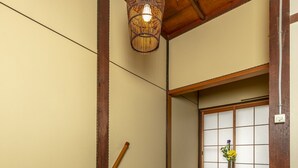 Een traditionele Japanse kamer met tatami vloeren, een houten balkenplafond en een hanglamp.