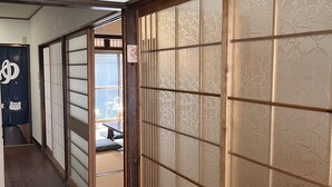 Een gang met schuifdeuren, houten vloeren en een zicht op een kamer met tatami-matten.