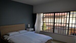 A hotel room with a bed, a nightstand, a lamp, and a window with a view of the outside.